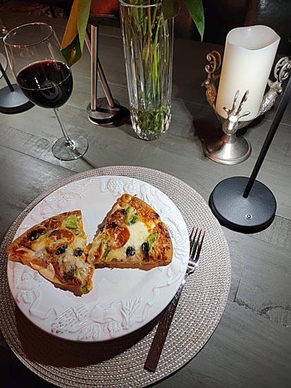 Pizza on pretty plate with fork, candle, wine and attractive place setting